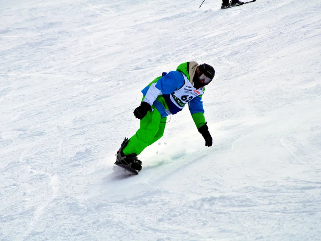 Snowboarder in grüner Hose in tiefer Hocke.
